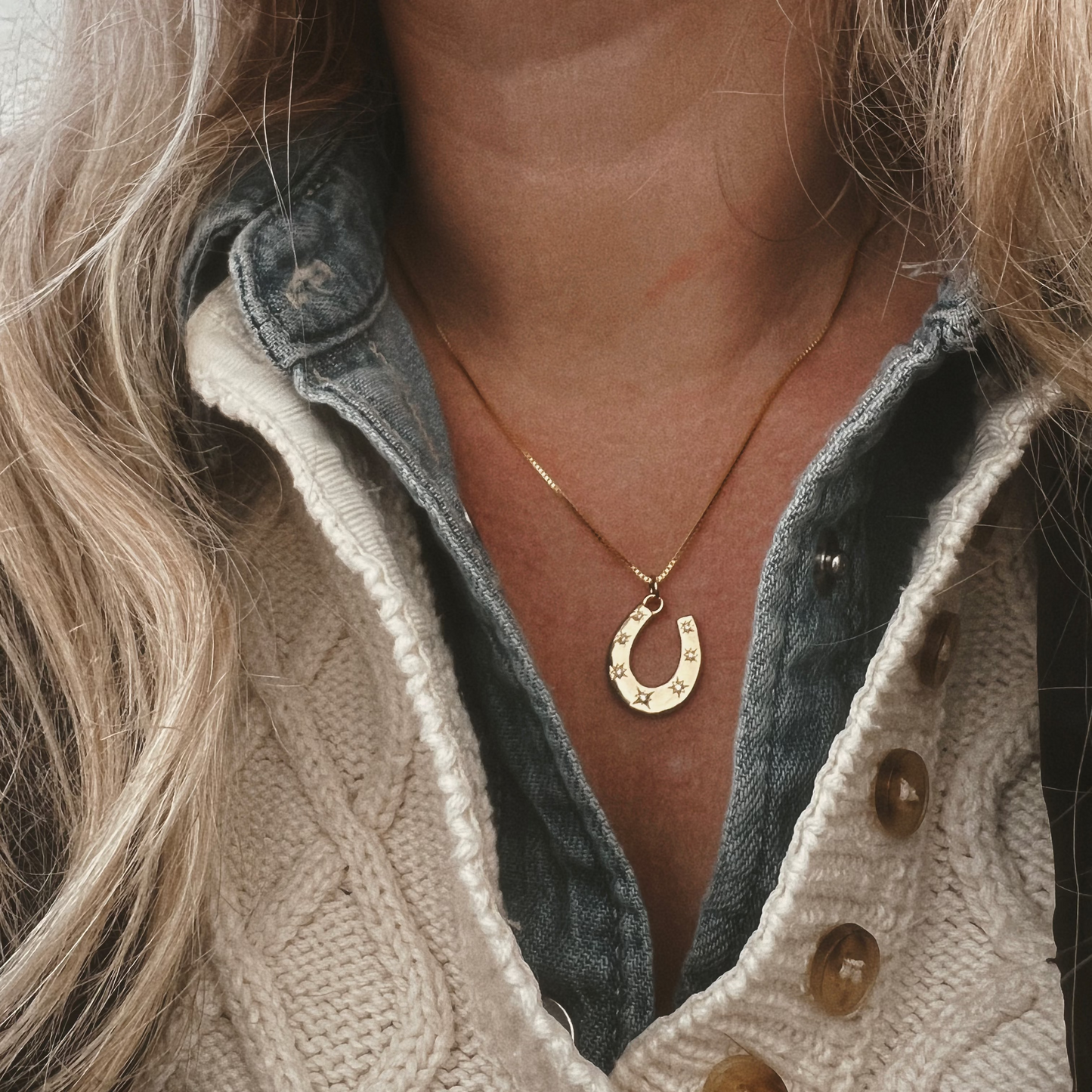 Close-up of a person wearing a gold horseshoe necklace  pendant.